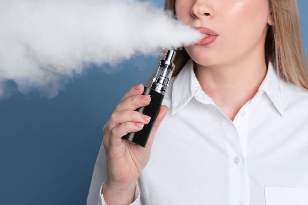 Young woman using electronic cigarette on light blue background, closeup